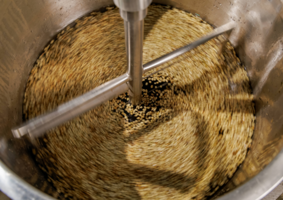 Overhead view of green coffee beans being stirred in water inside a cylindrical stainless steel tank