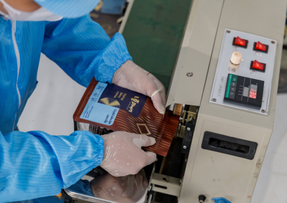 Worker wearing gloves guides a LOPHA coffee bag through a heat-sealing machine